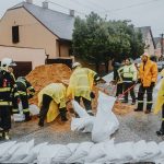 Equipe de emergência enche sacos de areia em uma rua sob chuva para ajudar a conter alagamentos.