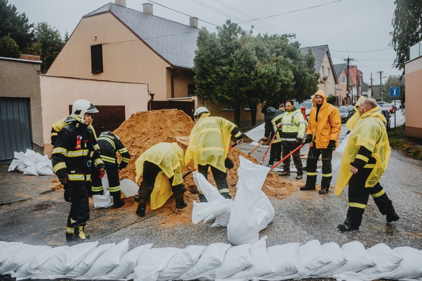 Equipe de emergência enche sacos de areia em uma rua sob chuva para ajudar a conter alagamentos.
