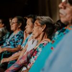 Pessoas idosas sentadas em um auditório, acompanhando atentamente uma atividade ou palestra