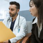Profissional de saúde conversa com uma paciente e analisa seus registros em um ambiente clínico.