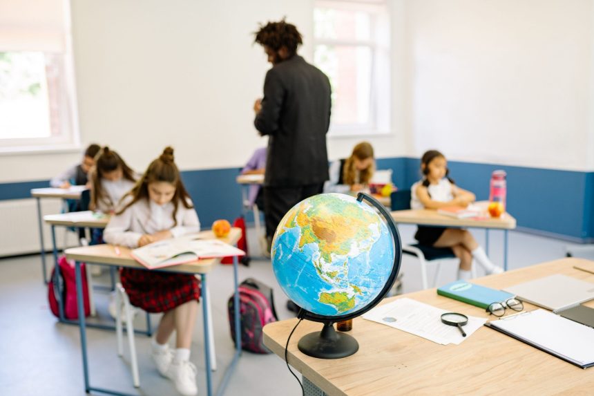 Estudantes em uma sala de aula durante uma atividade de geografia, com um globo sobre a mesa do professor.