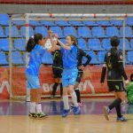 Jogadoras de futsal feminino comemoram juntas durante uma partida em quadra coberta.