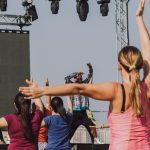 Grupo de pessoas participa de uma aula de zumba ao ar livre, acompanhando os movimentos de uma instrutora.
