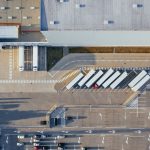 Vista aérea de um centro logístico com galpões, caminhões e estacionamento.
