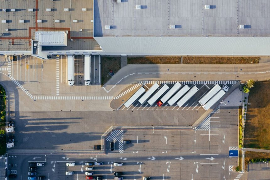 Vista aérea de um centro logístico com galpões, caminhões e estacionamento.