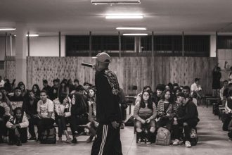 Artista de hip-hop se apresenta diante de uma plateia de estudantes em um espaço cultural.
