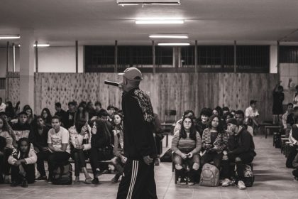 Artista de hip-hop se apresenta diante de uma plateia de estudantes em um espaço cultural.