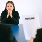 Mulher participa de uma entrevista de emprego diante de dois entrevistadores, com o currículo à sua frente.