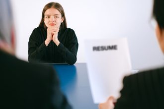 Mulher participa de uma entrevista de emprego diante de dois entrevistadores, com o currículo à sua frente.