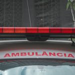 Close da dianteira de uma ambulância urbana, com a luz de emergência vermelha e a inscrição “AMBULÂNCIA”.