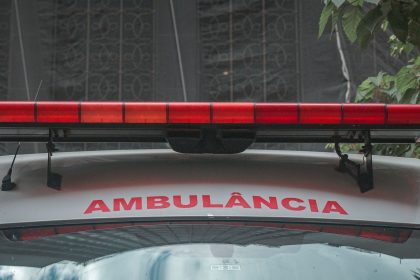 Close da dianteira de uma ambulância urbana, com a luz de emergência vermelha e a inscrição “AMBULÂNCIA”.