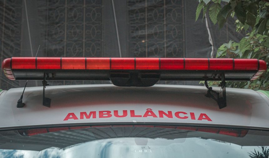 Close da dianteira de uma ambulância urbana, com a luz de emergência vermelha e a inscrição “AMBULÂNCIA”.